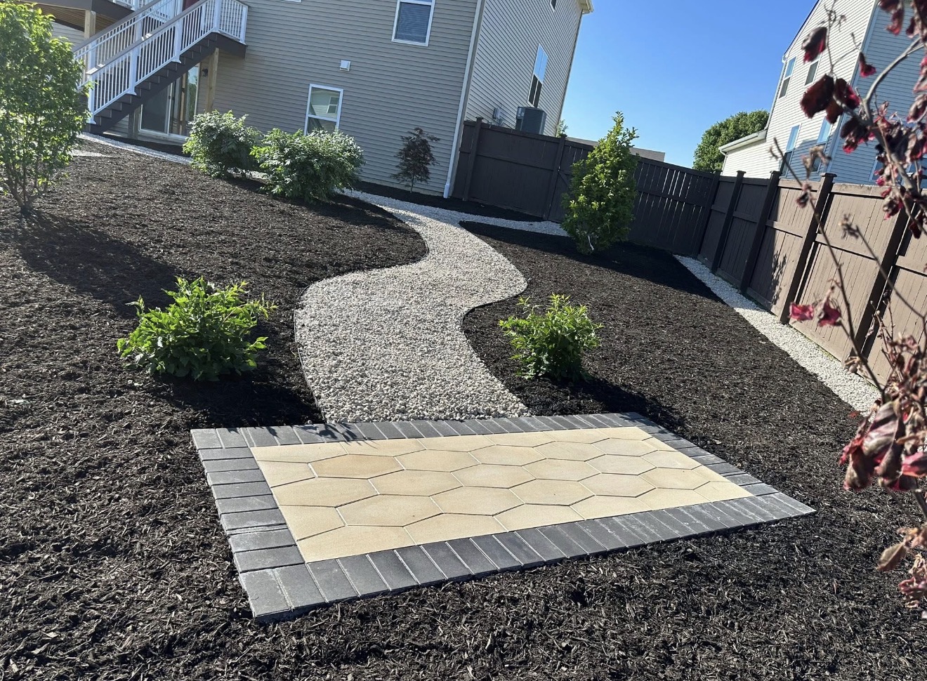 Mulched landscape with gravel pathway and decorative paver pad